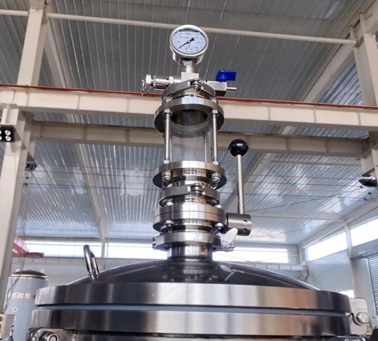 Stainless steel tank with pressure gauge and valve in an industrial setting.