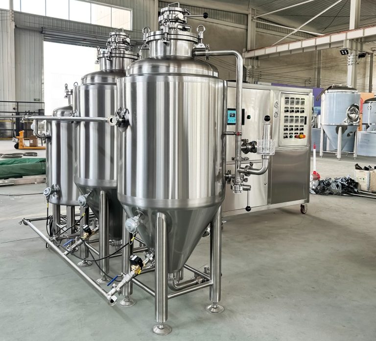 Three stainless steel fermentation tanks in a factory setting.