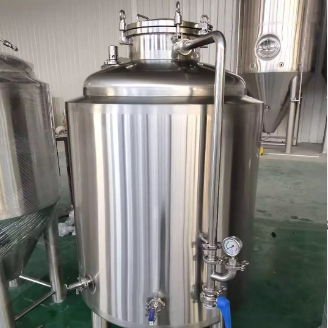 Stainless steel brewing vessel with pipes and valves in an industrial setting.