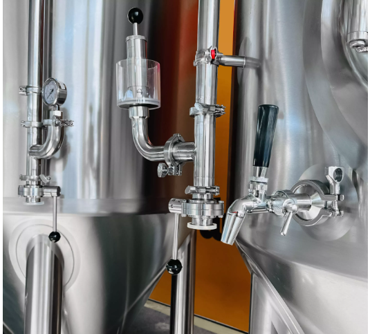 Stainless steel tank with pressure gauge and valve in an industrial setting.