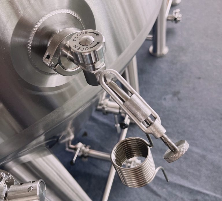 Three stainless steel fermentation tanks in a factory setting.