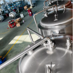 Metal storage tanks in a spacious industrial facility with equipment in the background.