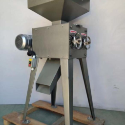 Industrial grain grinder with a hopper and motor, mounted on a wooden pallet.