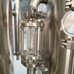 Close-up of a stainless steel valve with a glass viewing chamber and control levers.