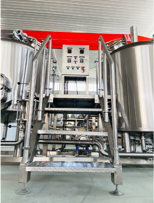 Metal stairs lead to a processing area with large stainless steel tanks and control panel.