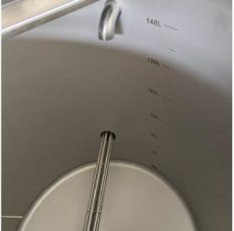 Stainless steel tank with measurement markings and a drain pipe at the bottom.