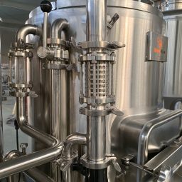 Close-up of a stainless steel brewing vessel with intricate piping and valves.