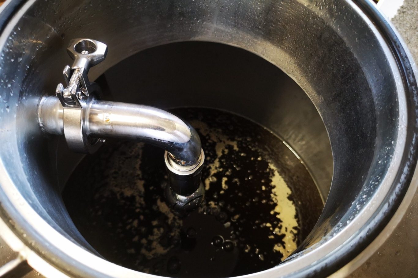 A stainless steel fermentation tank with a CIP arm and pre-fermented wort inside.